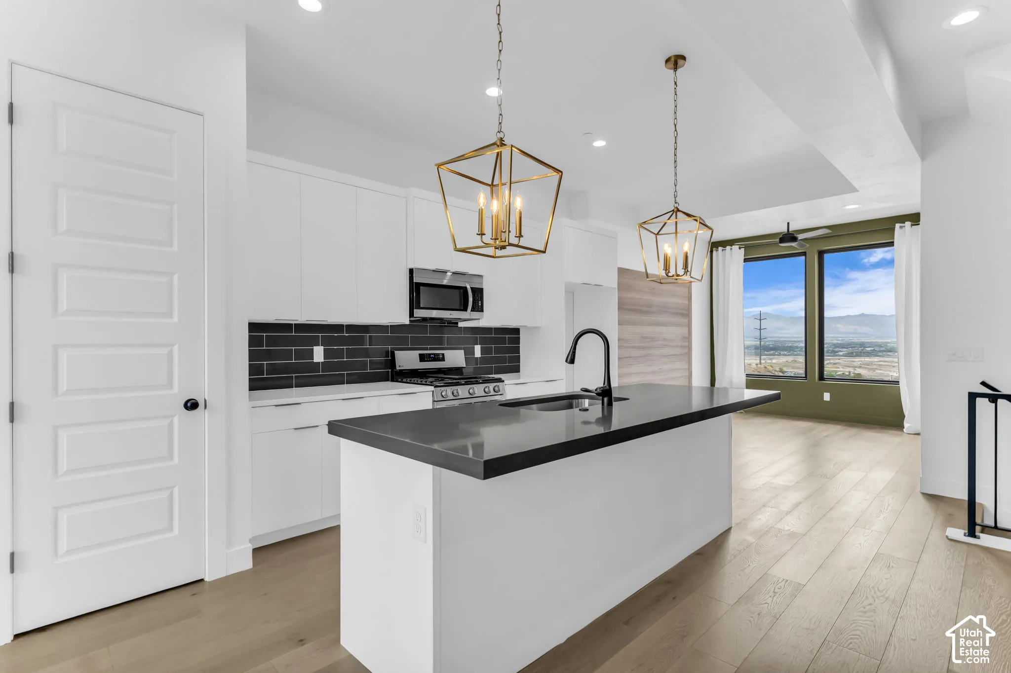 White flat-panel cabinetry, dark subway tile backsplash, and a central island with a black countertop and sink