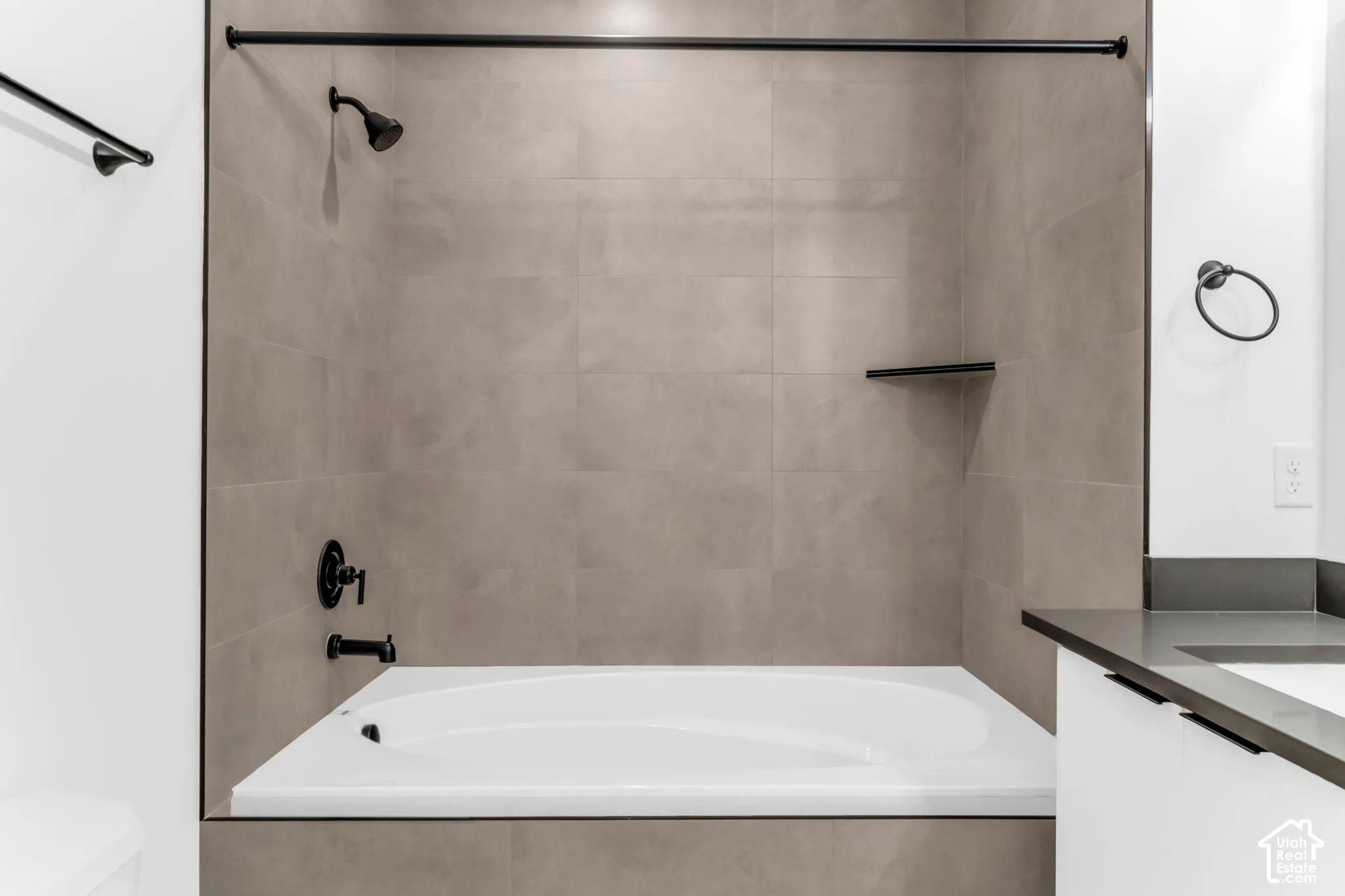 Bathtub with matte black fixtures, integrated shower head, built-in shelf, and large format wall tiling