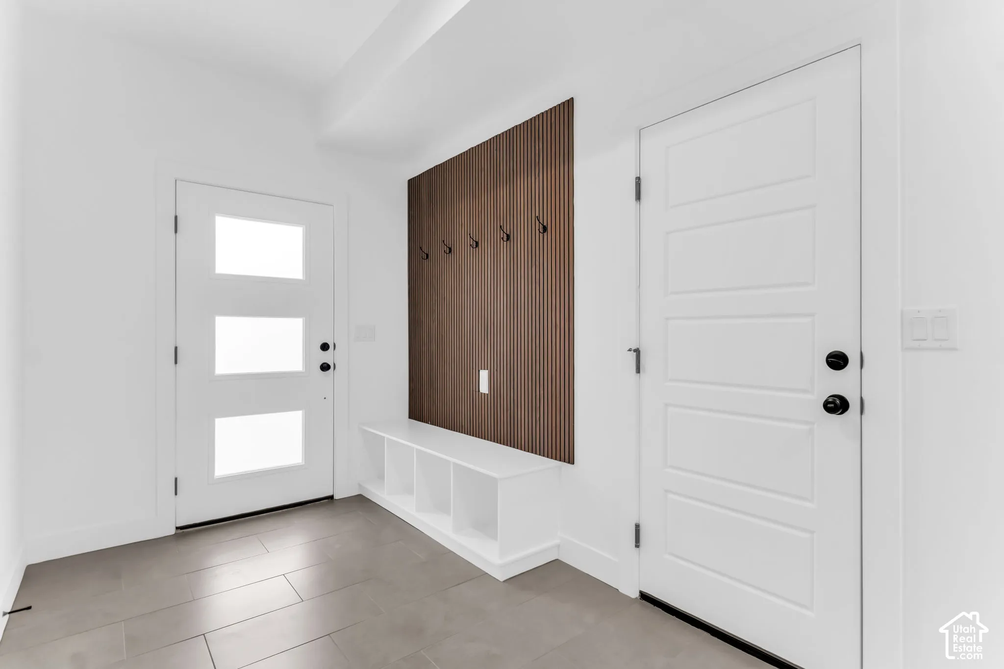 Entryway featuring tile flooring, a built-in bench with open storage, a wood-slat accent wall with wall-mounted hooks, and a door with frosted glass panels