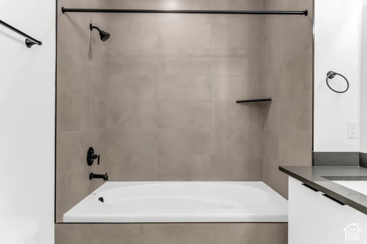 Bathtub with matte black fixtures, integrated shower head, built-in shelf, and large format wall tiling