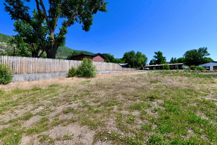 Expansive land parcel featuring a wooden privacy fence, established trees, and a mountain backdrop