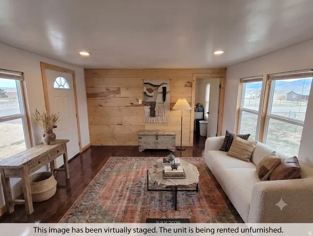 Hardwood flooring, recessed lighting, wood-paneled accent wall, multiple windows, and a paneled entry door with an arched transom