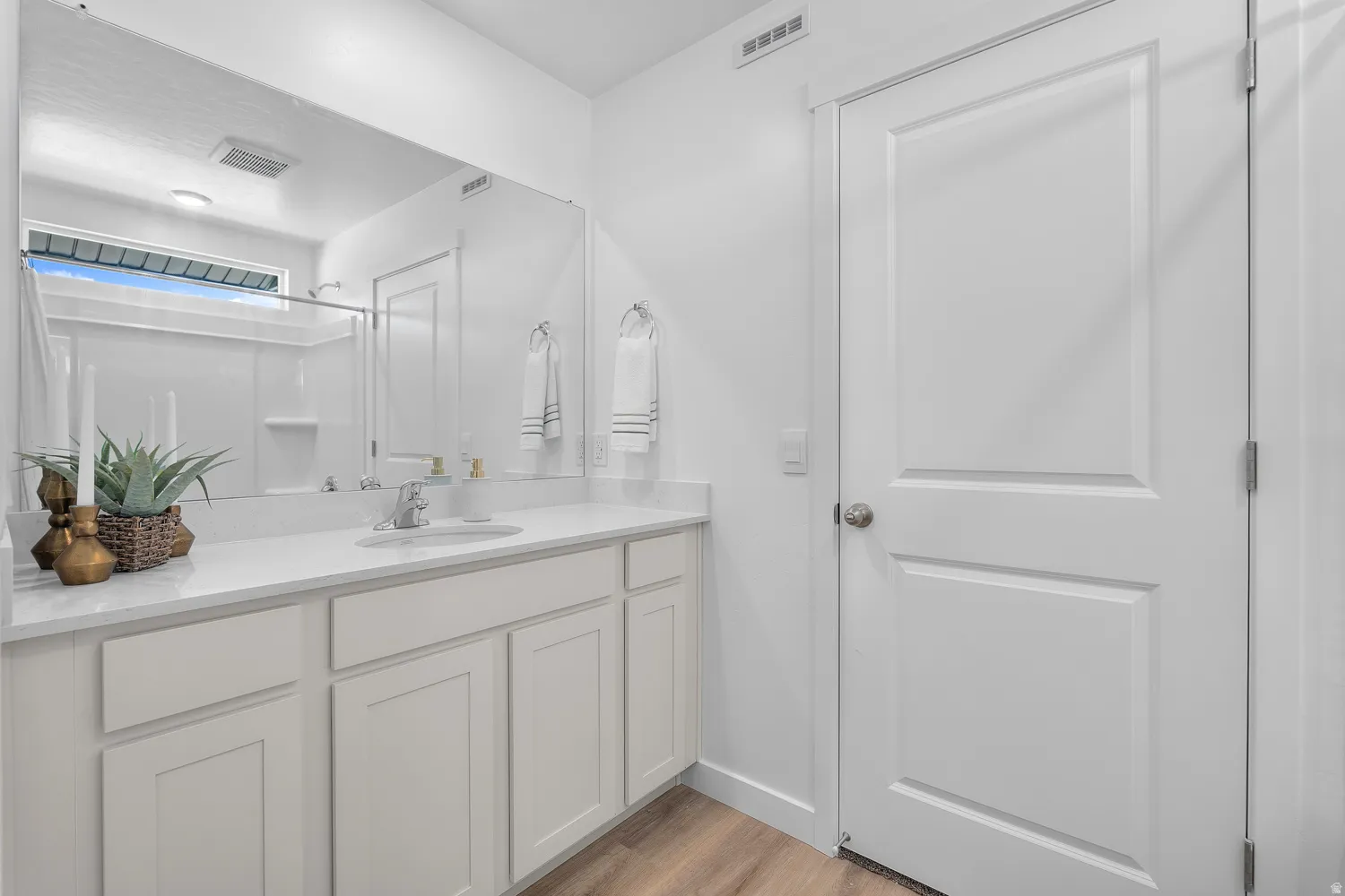 White shaker-style cabinetry, a white countertop, an undermount sink, a large wall-mounted mirror, and wood-finish flooring