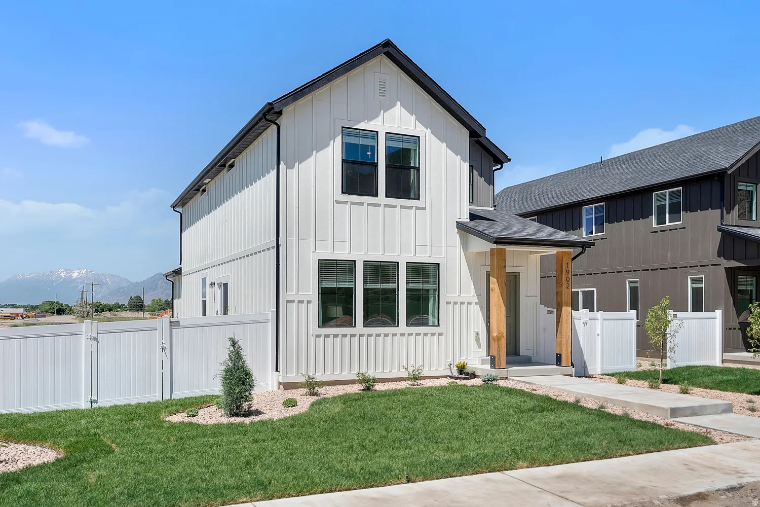 Modern farmhouse exterior with vertical white siding, black-framed windows, dark roof, and a covered entryway with natural wood columns
