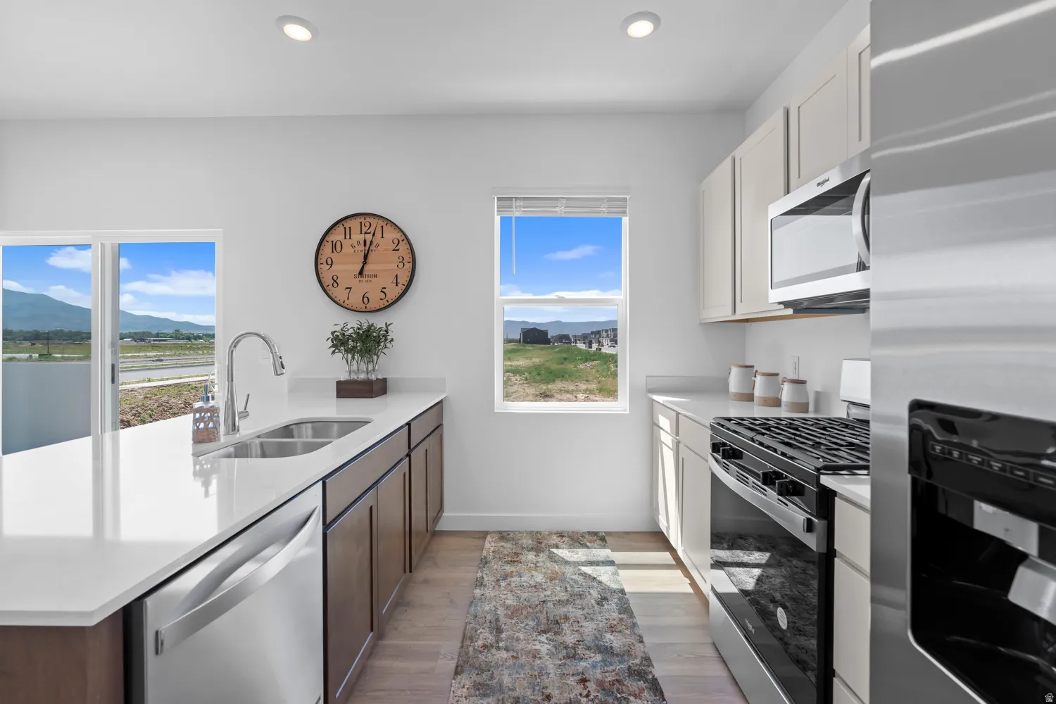 Kitchen featuring recessed lighting, a stainless steel sink, white countertops, wood-finish lower cabinetry, and light-toned upper cabinetry