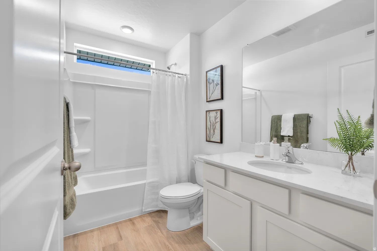 White vanity with a single basin sink, large mirror, wood-finish flooring, and a white bathtub with an overhead window