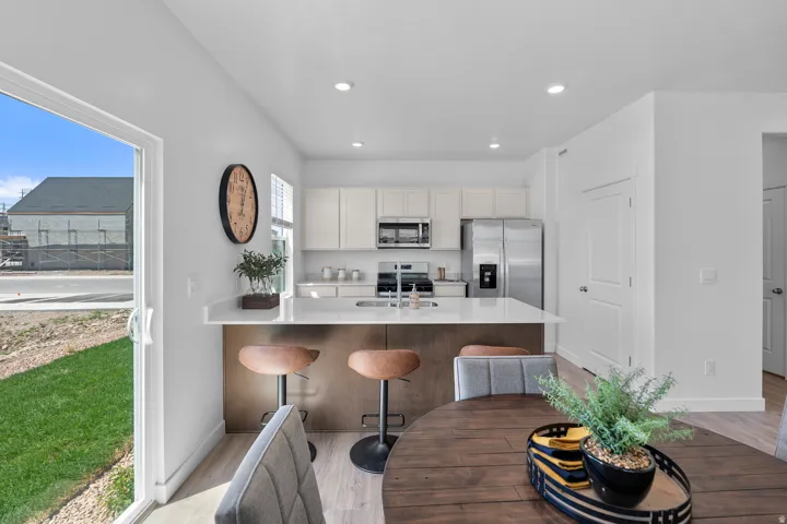 Open-concept kitchen and dining area featuring white cabinetry, stainless steel appliances, a center island with countertop seating, and recessed lighting