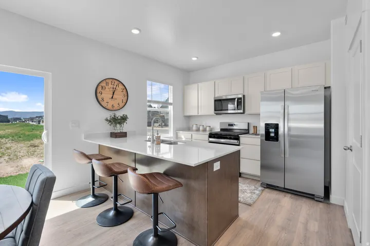 Kitchen featuring light wood-finish flooring, white cabinetry, stainless steel appliances, a center island with a light-colored countertop, and a sliding glass door
