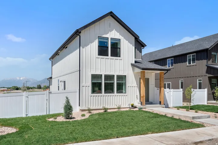 Modern farmhouse exterior with vertical white siding, black-framed windows, dark roof, and a covered entryway with natural wood columns