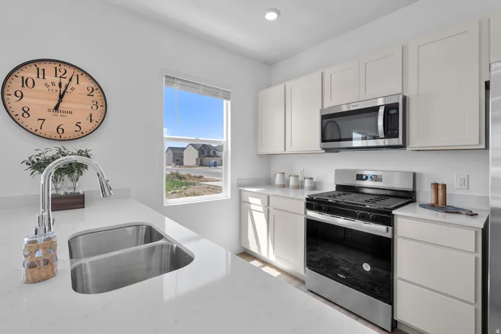 White shaker-style cabinetry, stainless steel appliances, dual-basin sink with a gooseneck faucet, light-toned countertops, and an integrated microwave