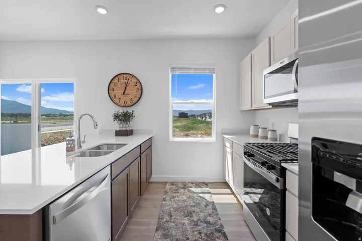 Kitchen featuring recessed lighting, a stainless steel sink, white countertops, wood-finish lower cabinetry, and light-toned upper cabinetry