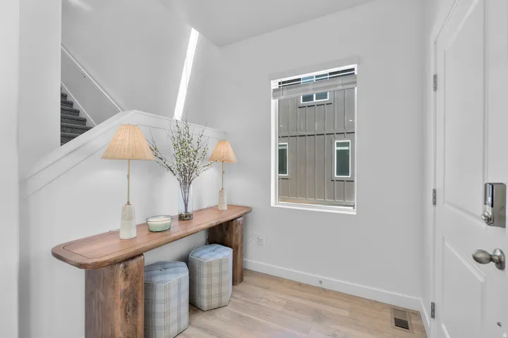 Light wood-finish flooring, staircase with carpeted treads, white painted walls, and a window with blinds