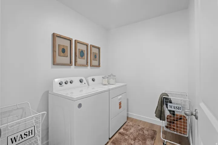 Dedicated laundry area featuring a washer and dryer, light-toned walls, and wood-finish flooring