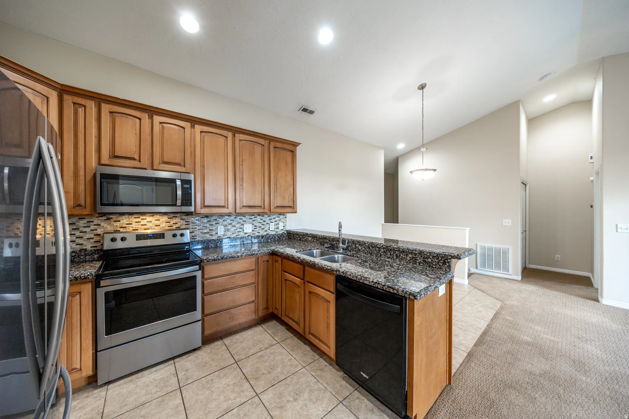 Kitchen featuring warm wood cabinetry, stainless steel appliances, mosaic tile backsplash, granite-style countertops, and a center island with seating