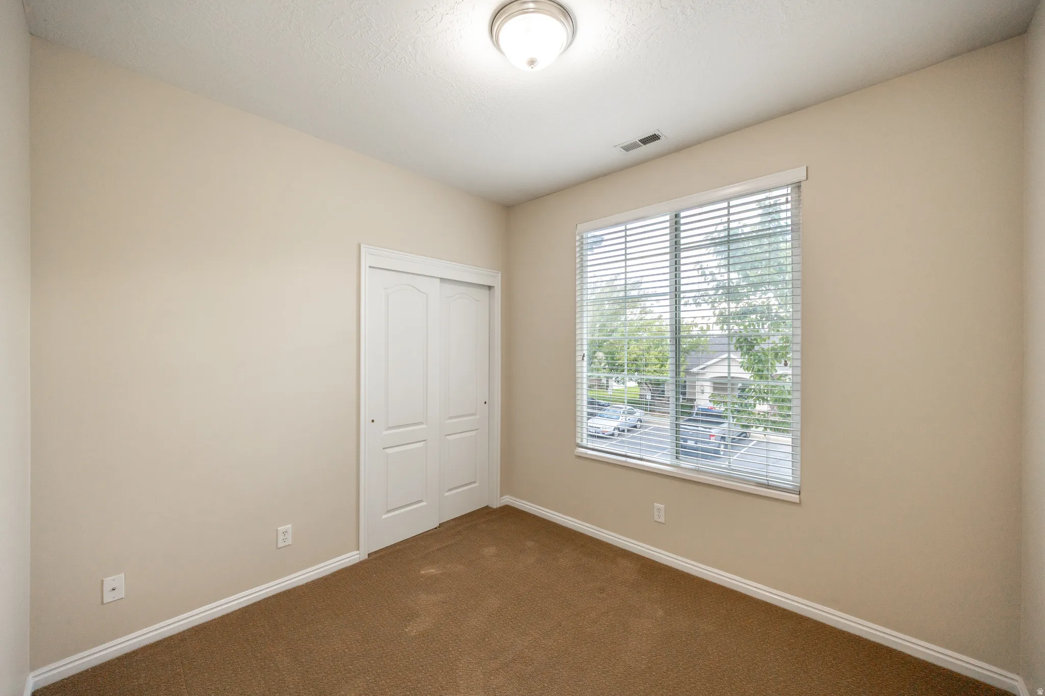 Neutral wall paint, brown carpet flooring, white window blinds, and a built-in closet with sliding panel doors