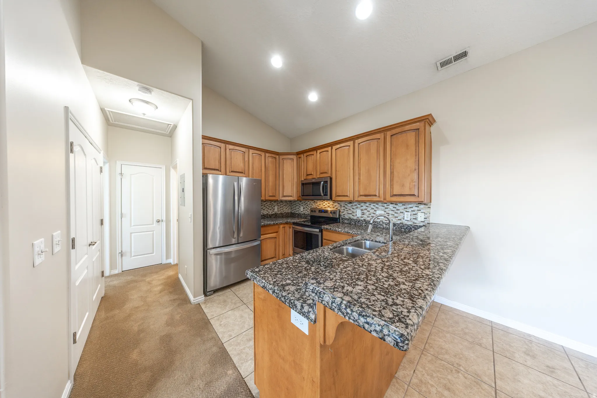 Kitchen featuring wood cabinetry, stainless steel appliances, a double basin sink, tile backsplash, and a granite countertop