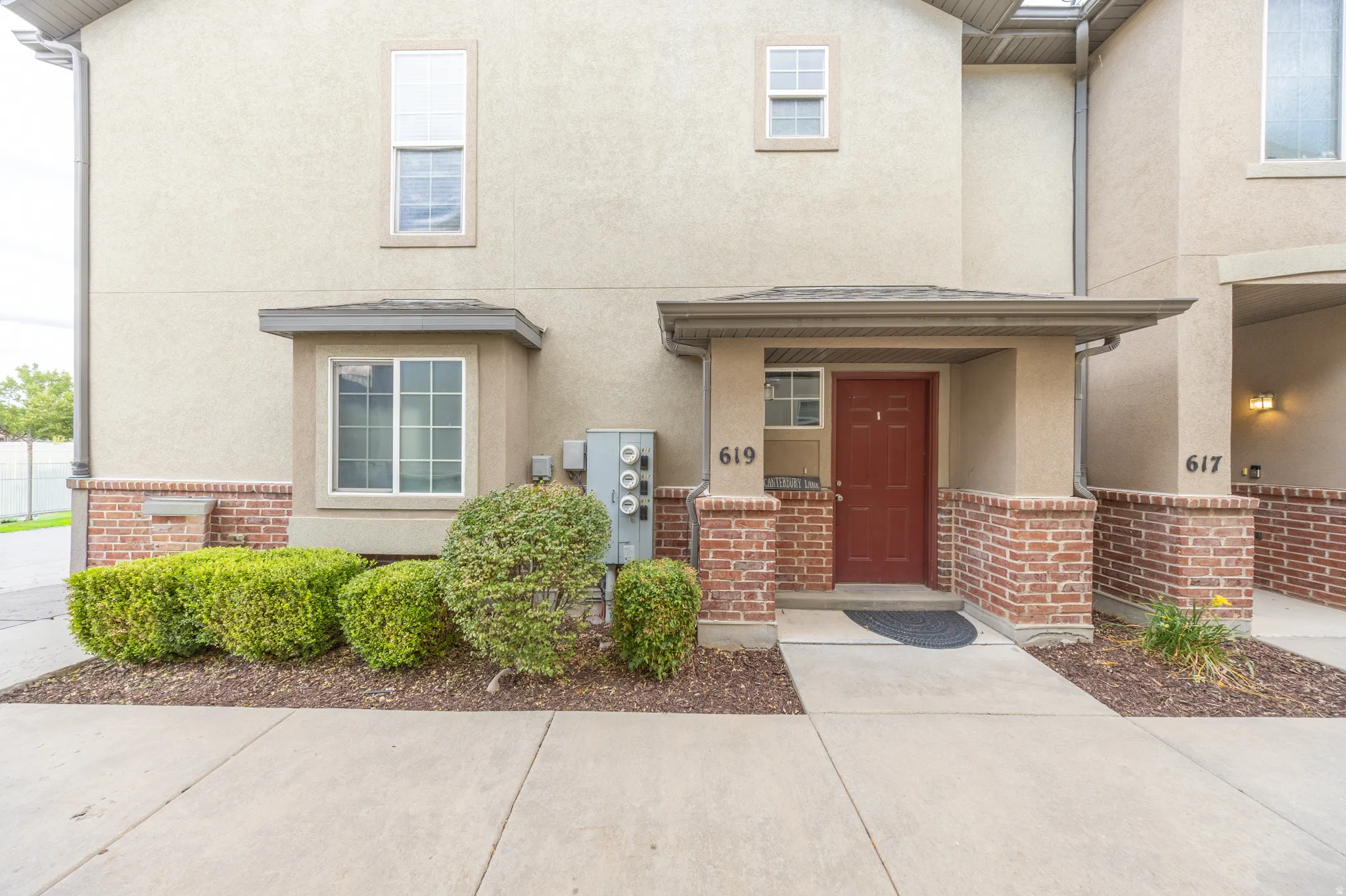 Stucco exterior with brick detailing, covered entryway, and a red panel door