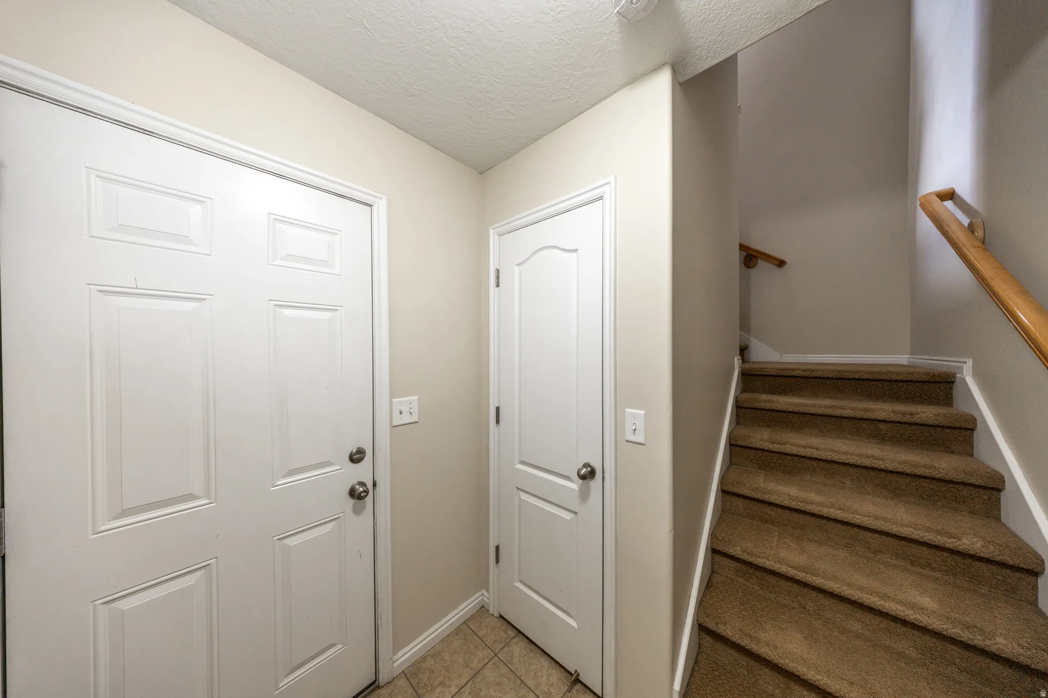 Staircase with wood handrail, beige wall paint, and tiled flooring