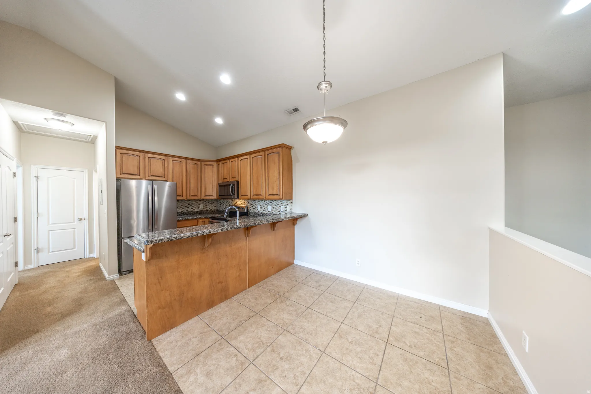 Kitchen featuring wood cabinetry, stainless steel appliances, a tiled backsplash, and a breakfast bar