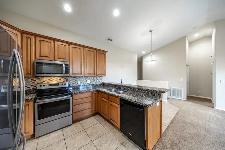 Kitchen featuring warm wood cabinetry, stainless steel appliances, mosaic tile backsplash, granite-style countertops, and a center island with seating