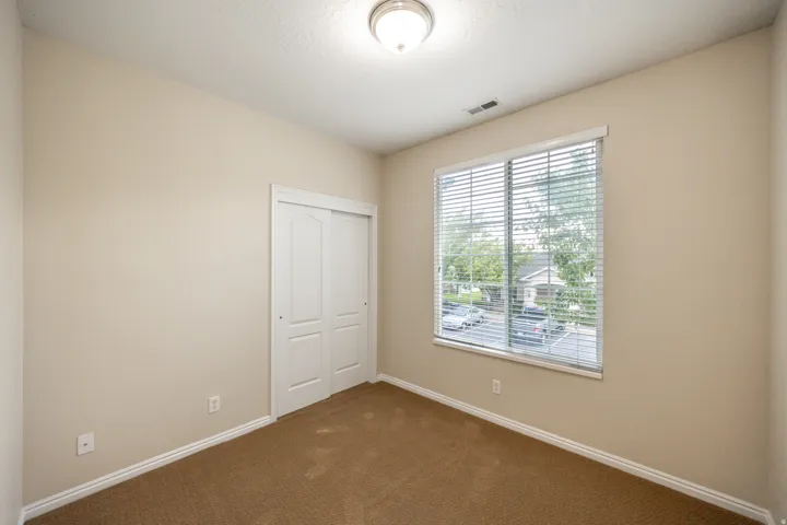 Neutral wall paint, brown carpet flooring, white window blinds, and a built-in closet with sliding panel doors