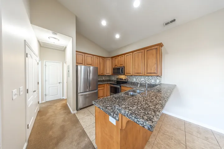 Kitchen featuring wood cabinetry, stainless steel appliances, a double basin sink, tile backsplash, and a granite countertop