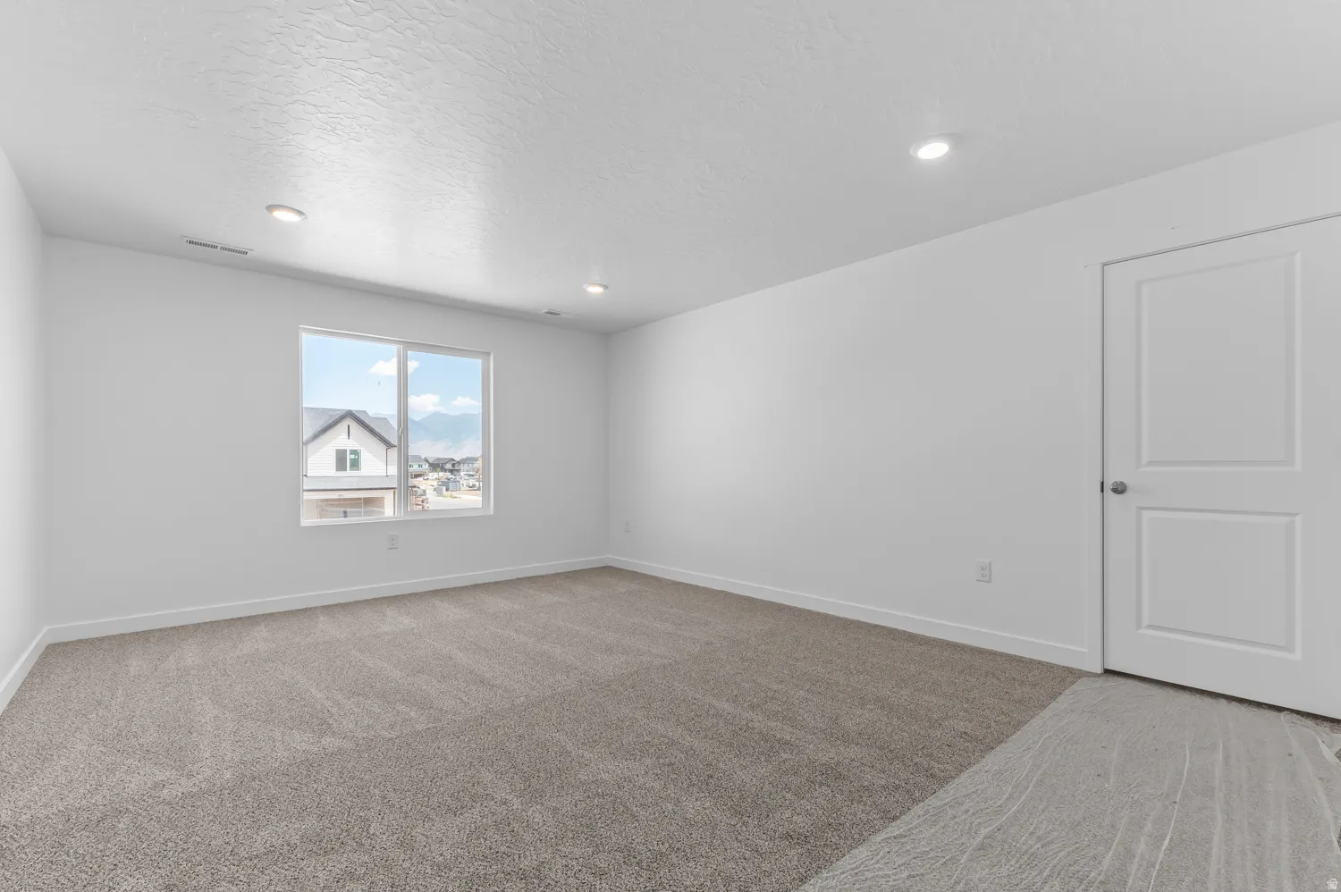 Recessed lighting, large window, neutral carpet, white paneled door, and white baseboards