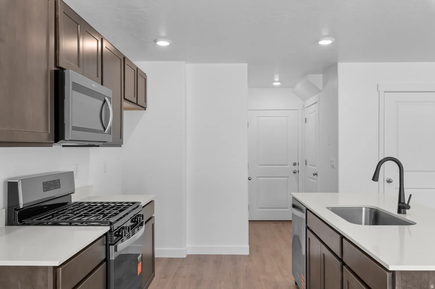 Kitchen featuring dark wood-finish cabinetry, light countertops, stainless steel appliances, and wood-finish flooring