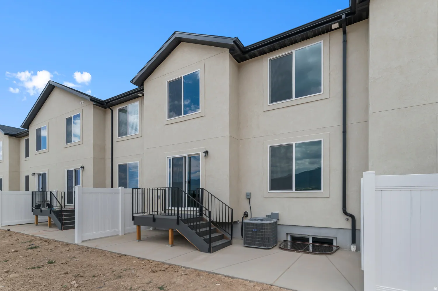 Stucco exterior with multiple windows, individual patio, rear deck with stairs, and white privacy fencing