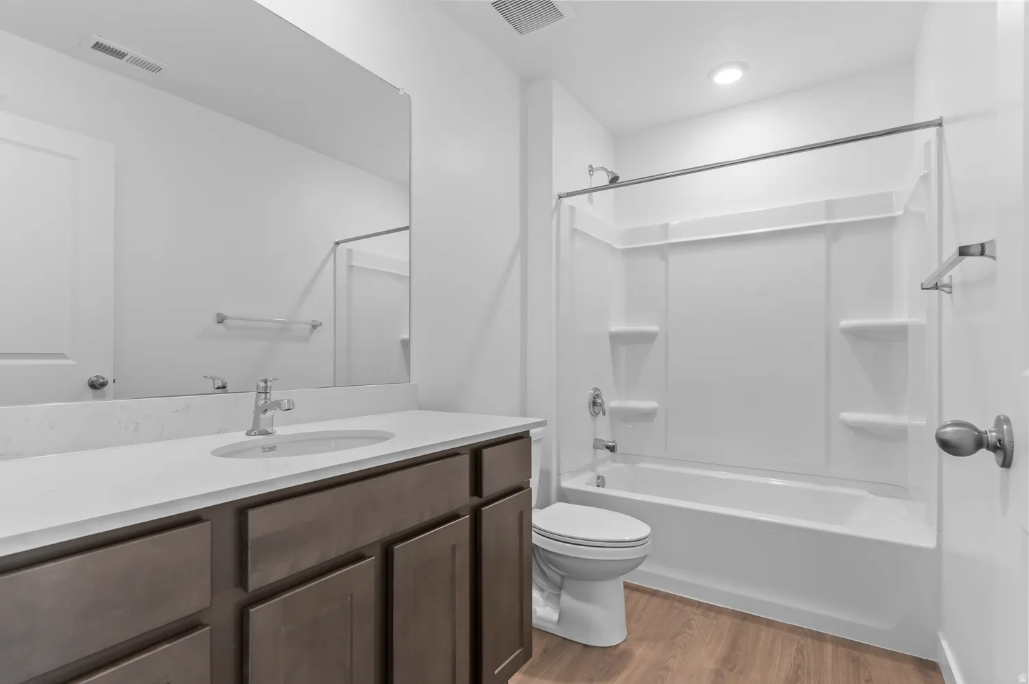 Wood-finish flooring, single vanity with light-colored countertop, undermount sink, and chrome faucet