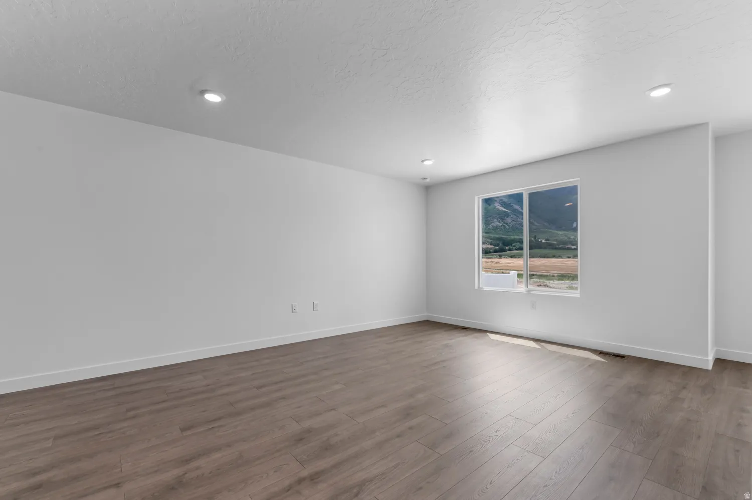 Spacious room featuring wood-finish flooring, recessed lighting, and a large window