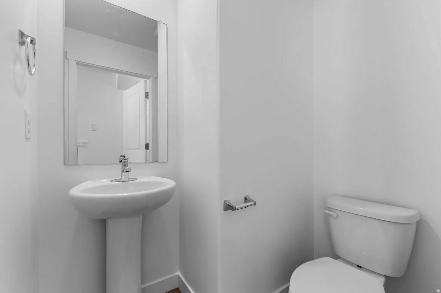 White pedestal sink with a chrome faucet, wall-mounted mirror, and a white toilet