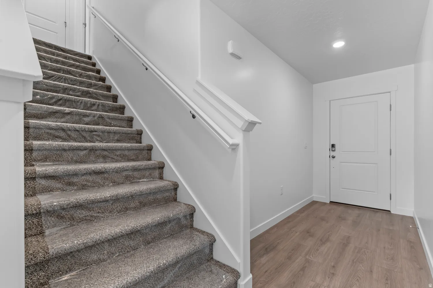 Carpeted staircase with white handrail and wood-finish flooring