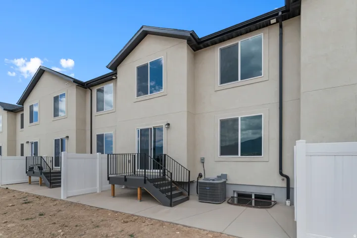 Stucco exterior with multiple windows, individual patio, rear deck with stairs, and white privacy fencing