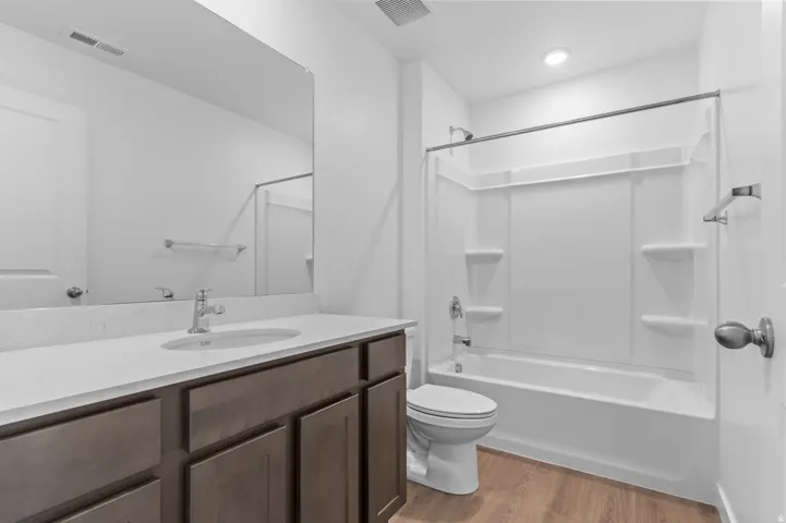 Wood-finish flooring, single vanity with light-colored countertop, undermount sink, and chrome faucet
