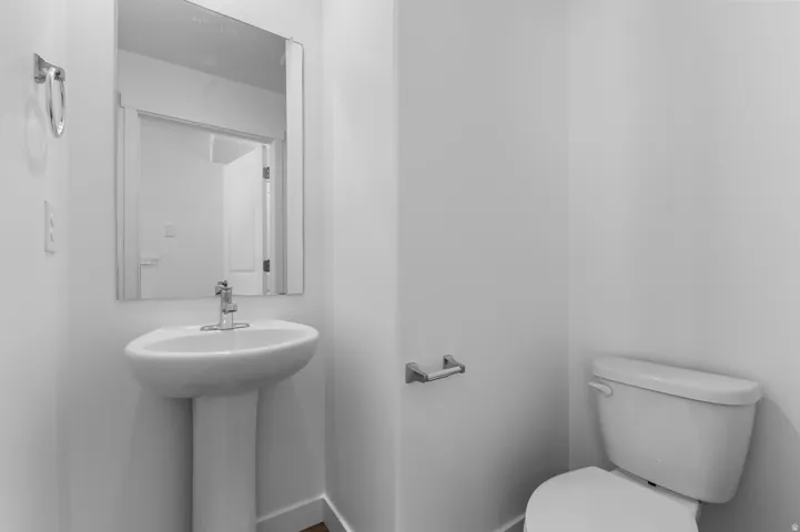 White pedestal sink with a chrome faucet, wall-mounted mirror, and a white toilet