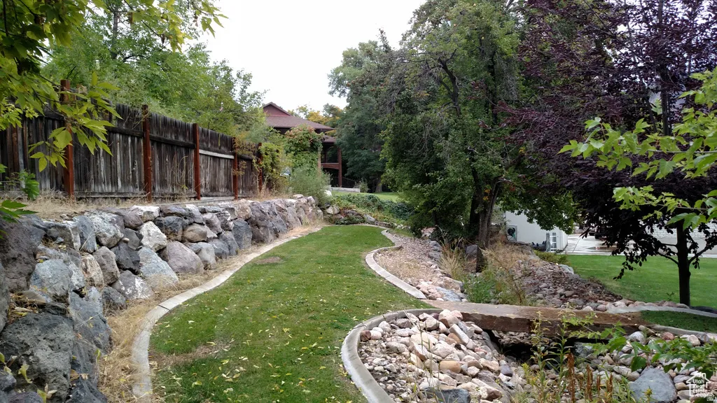 Landscaped grounds featuring a meandering lawn, natural stone retaining walls, mature trees, and a wooden fence