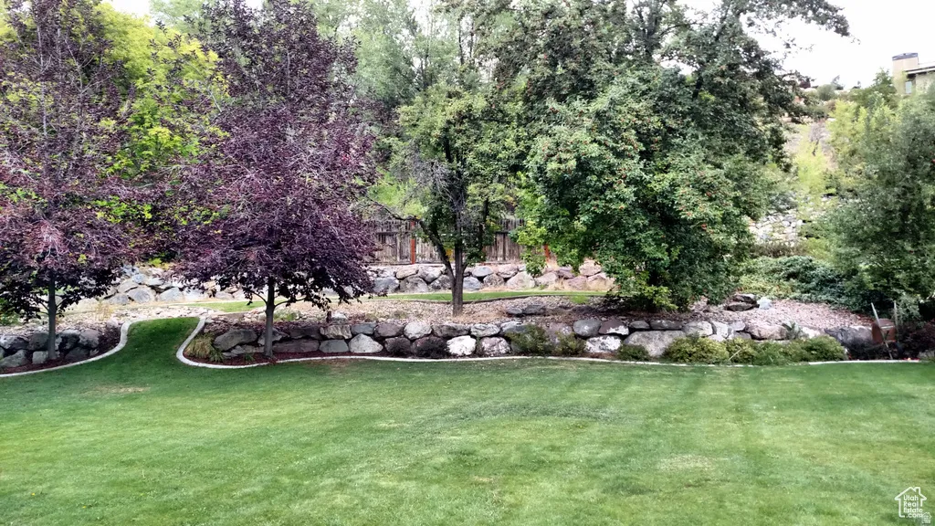 Expansive green lawn with a defined border, mature trees, and natural rock retaining walls