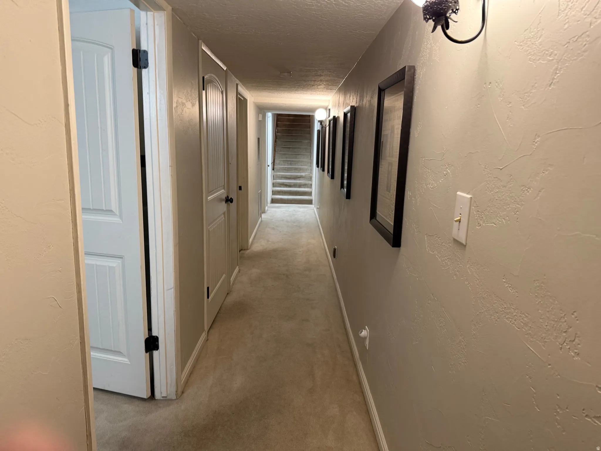 Hallway with textured walls, wall-mounted sconce lighting, and carpet flooring