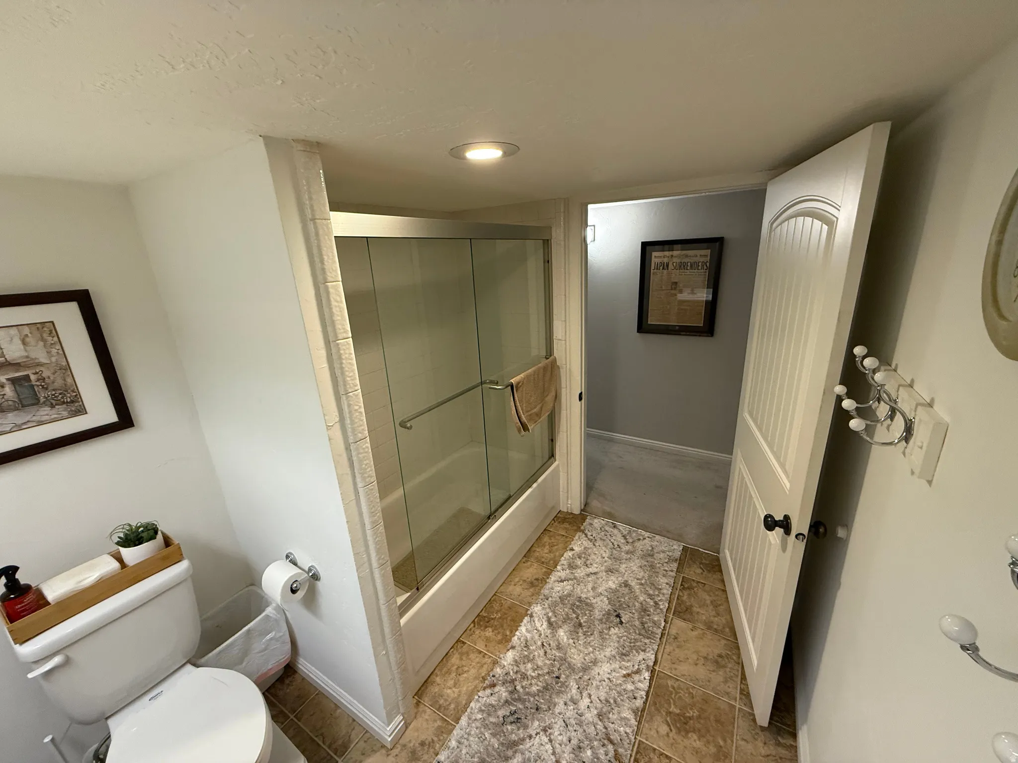 Tile flooring paired with a white toilet and a shower-over-tub combination featuring a glass enclosure