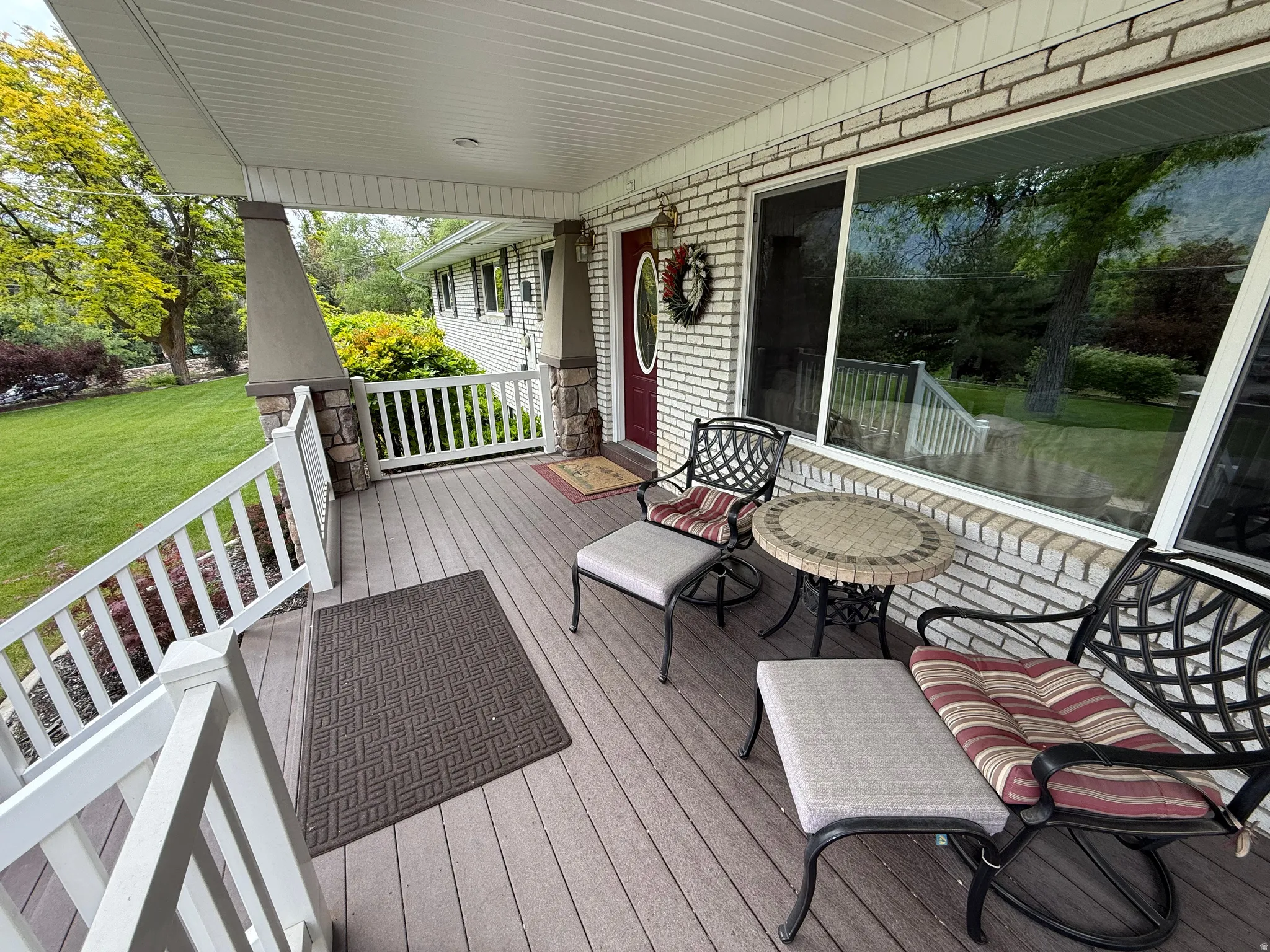 Covered porch with wood-finish decking, white brick exterior, and a red entry door
