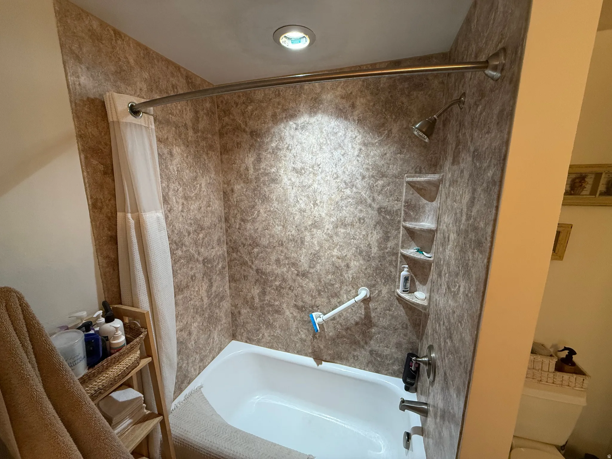 Bathtub with a shower combination featuring a built-in multi-level corner shelf, recessed lighting, and a grab bar