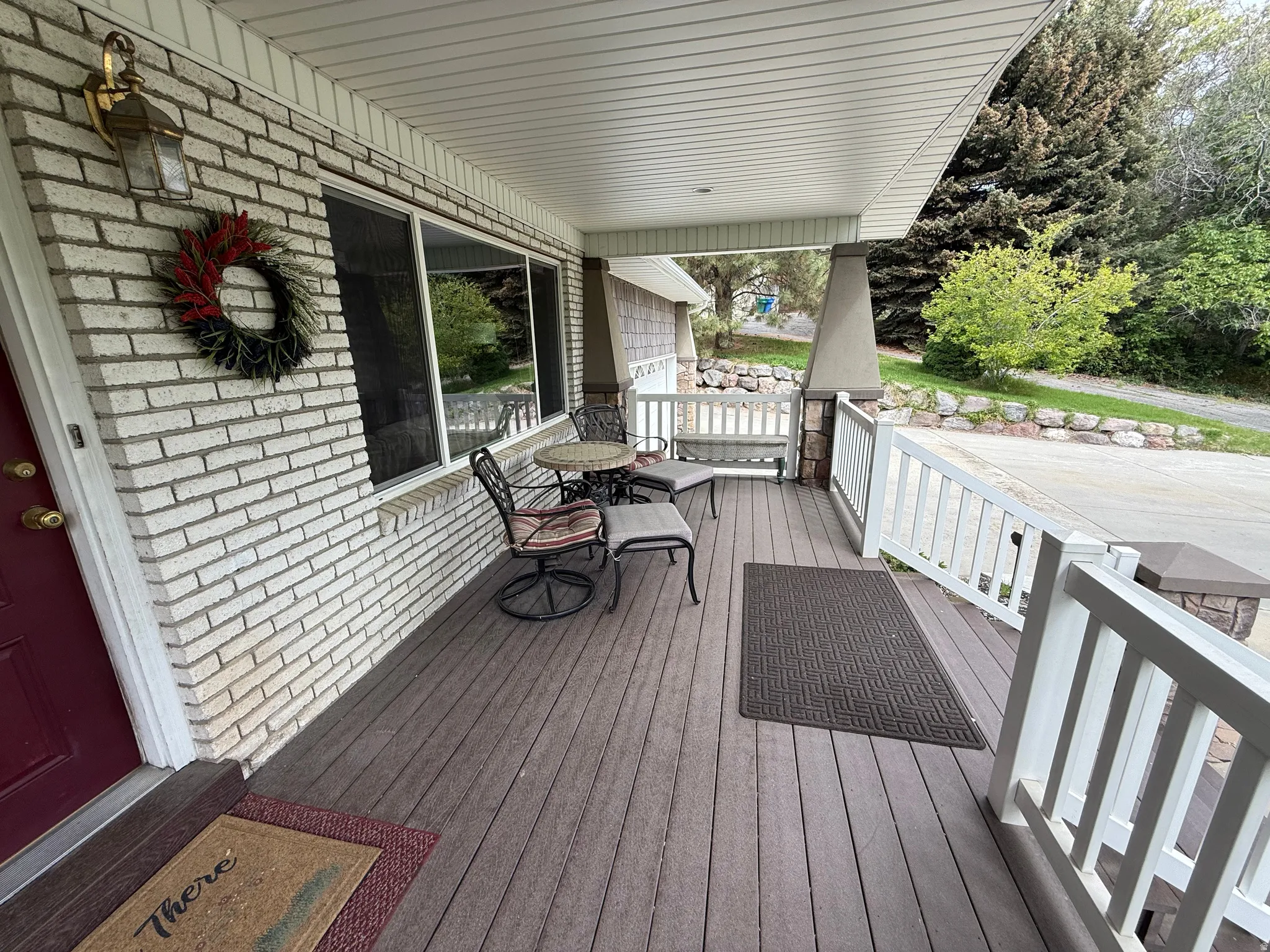 Covered front porch featuring a wood-finish deck, white brick exterior, and white railing