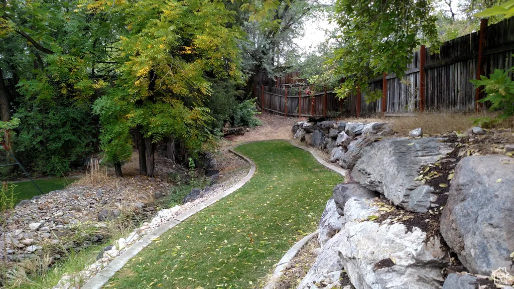 Tiered landscaping with a curved grass pathway, natural rock retaining walls, mature trees, and a wood fence border