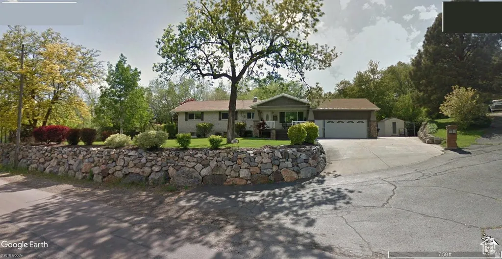 Stone retaining wall with mature landscaping, attached two-car garage, and paved driveway