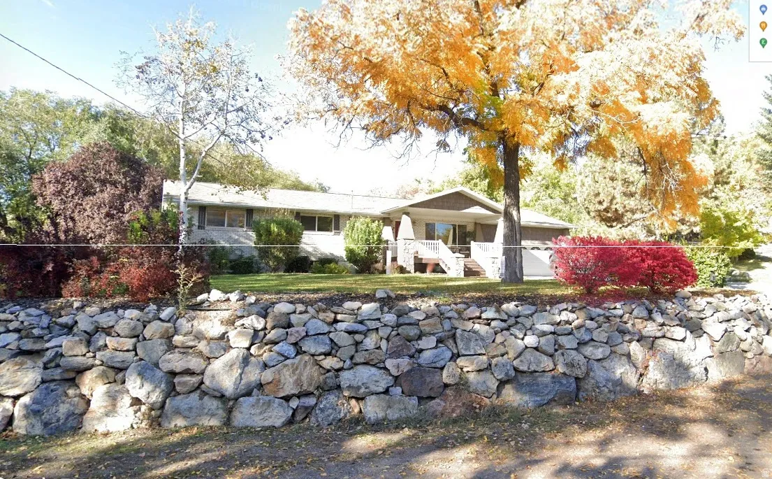 Stone retaining wall with established landscaping, mature trees, and a front porch entry