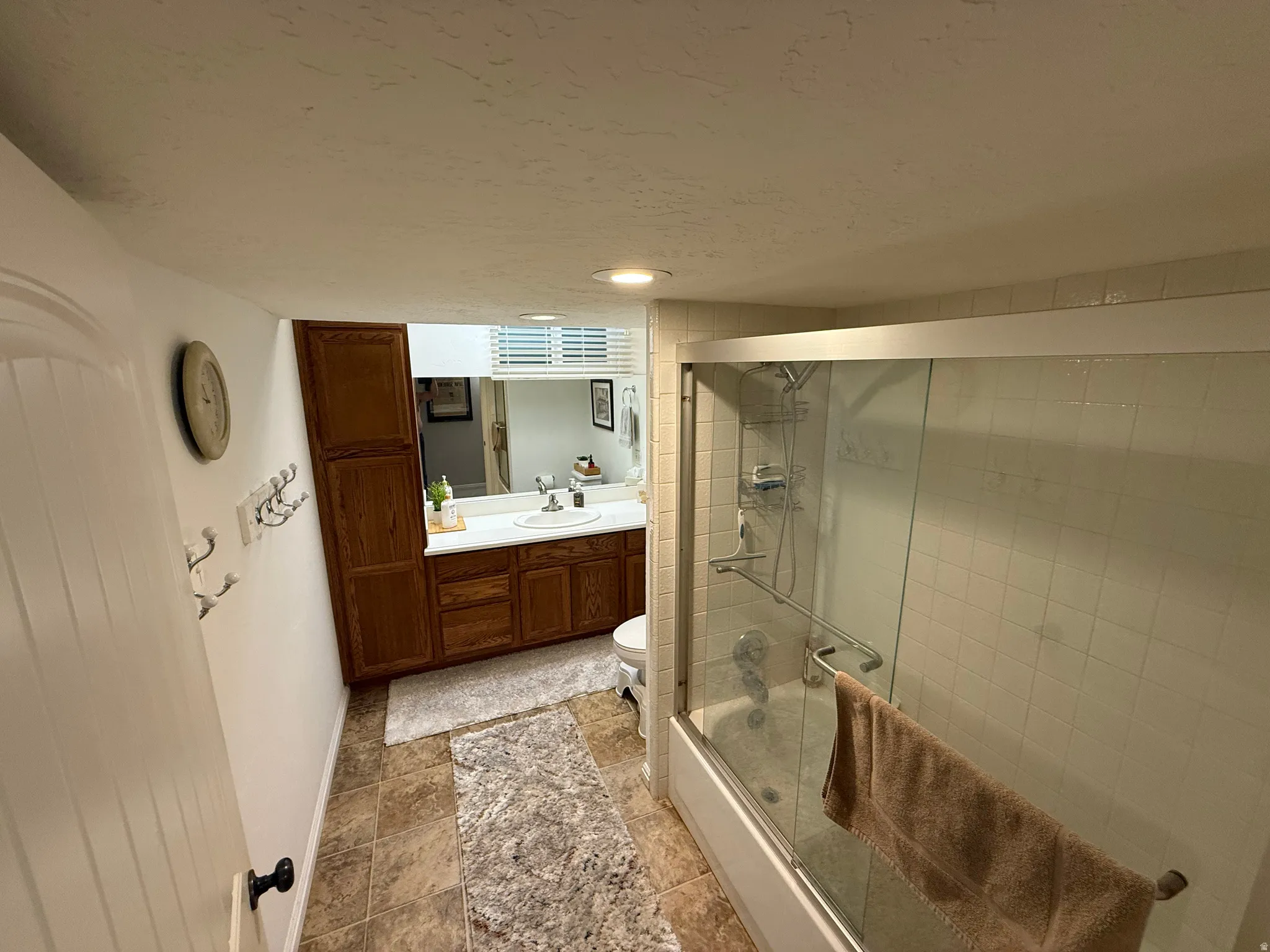 Tile flooring, wood-finish cabinetry, built-in bathtub with shower, glass shower enclosure, and a vanity with an integrated sink