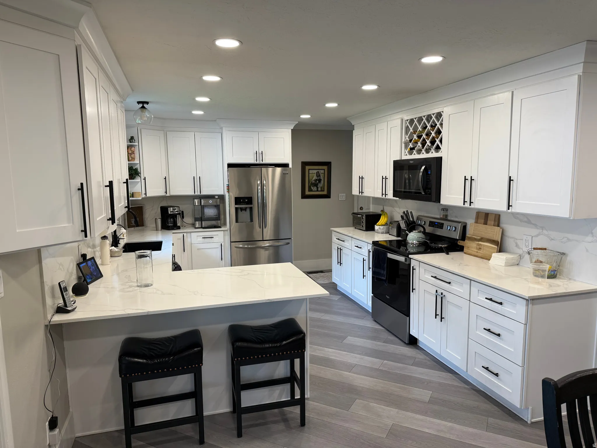 White shaker-style cabinetry with matte black hardware, integrated wine rack, stainless steel appliances, and light-toned countertops