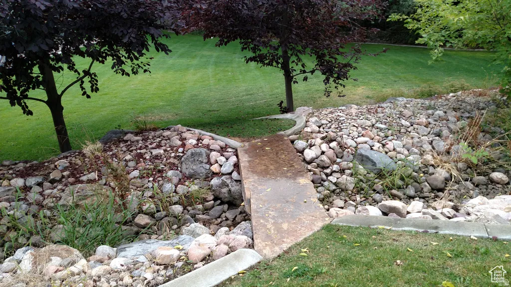Manicured lawn with mature trees and a decorative rock bed with a concrete walkway