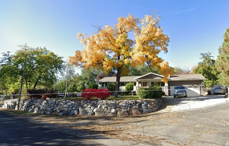 Ranch-style exterior with a stone retaining wall, mature landscaping, and an attached two-car garage